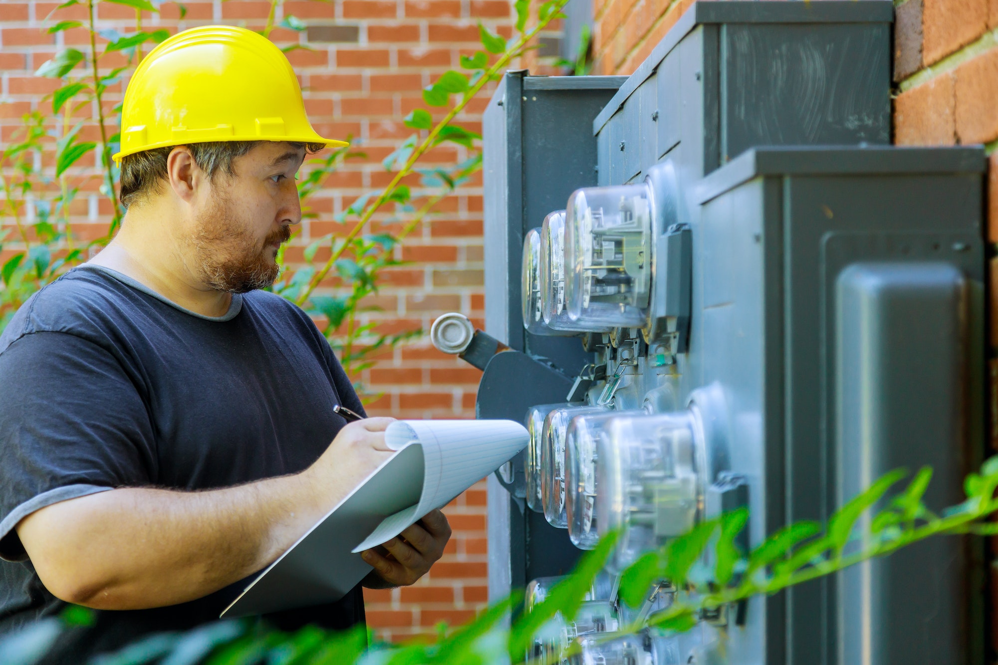 Technik elektryczny w żółtym kasku pisze odczyt licznika w schowku