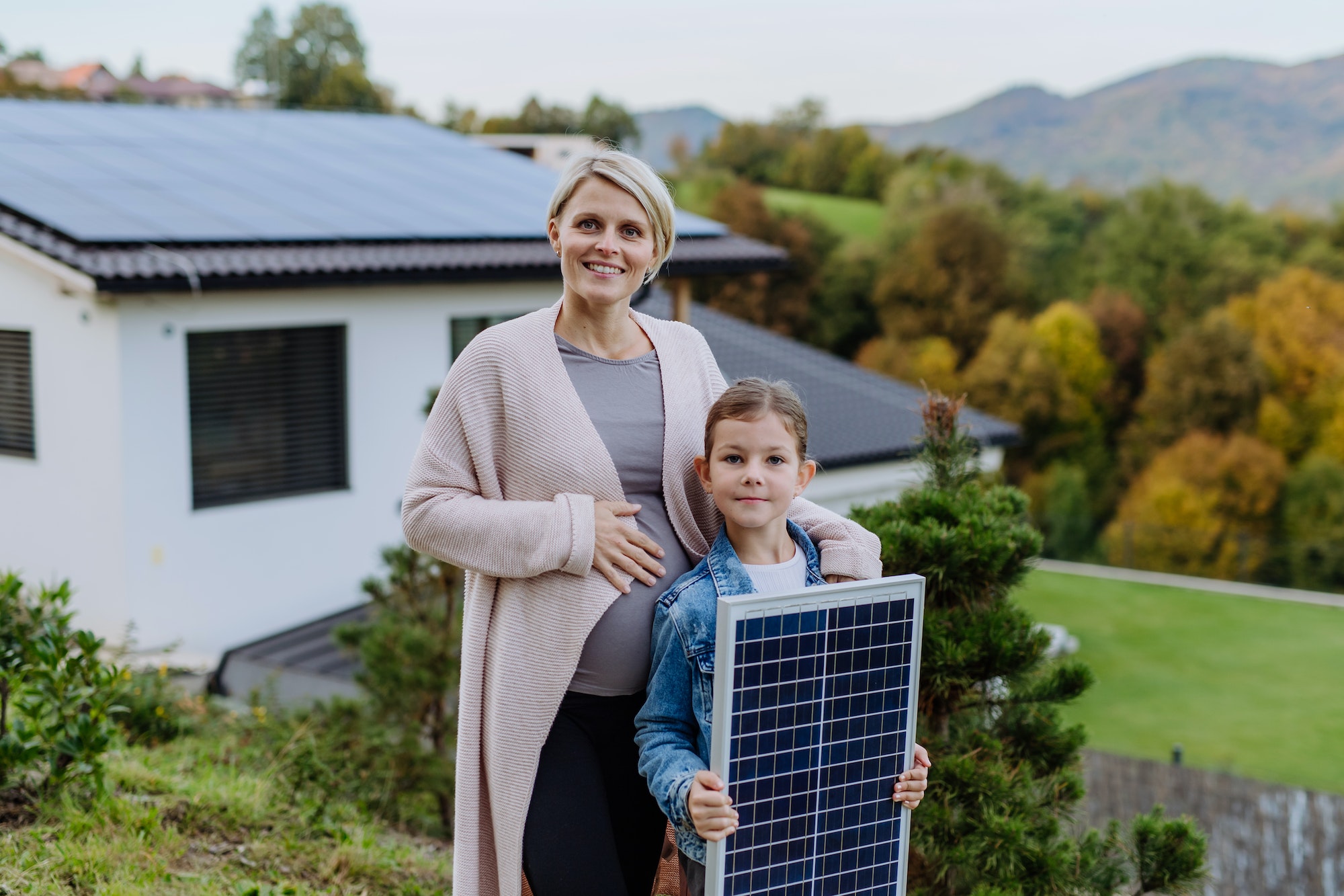 Matka z małą córeczką w pobliżu ich domu z panelami słonecznymi. Alternatywne źródła energii, oszczędność