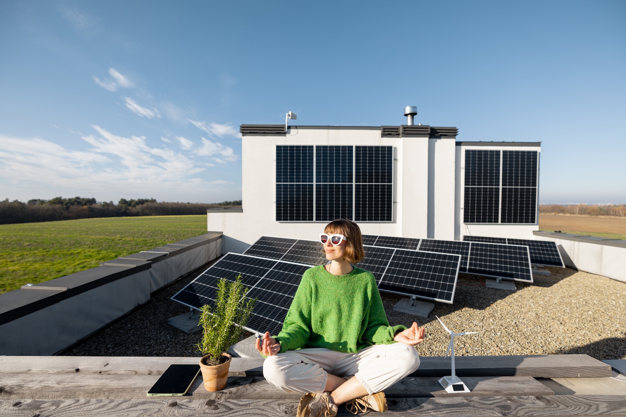 Woman meditates on rooftop of her house with solar power plant on background